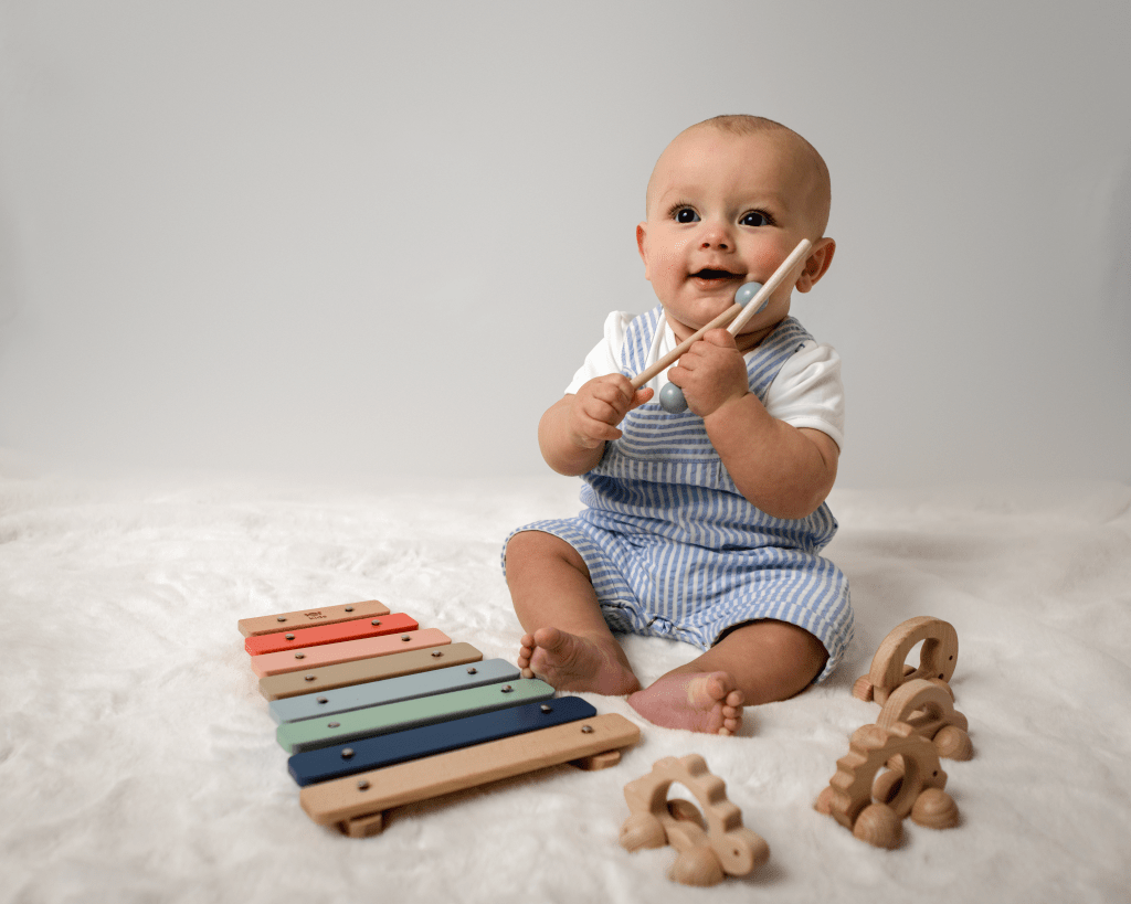 a baby sitting down smiling playing with a wooden xylophone