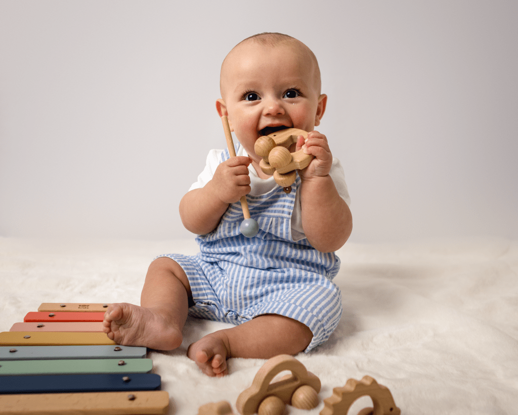 a baby sitting down chewing a wooden toy happily