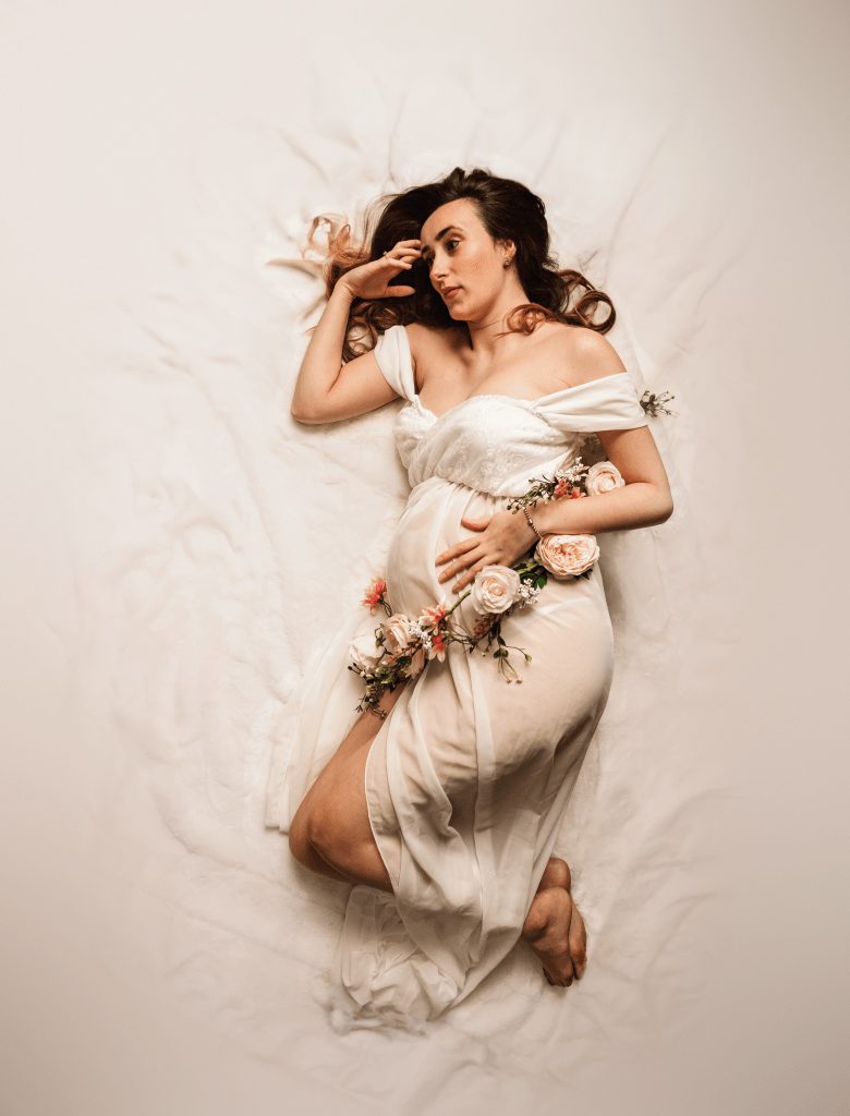 mother holding bump, laying down with a wrap of roses around her waist
