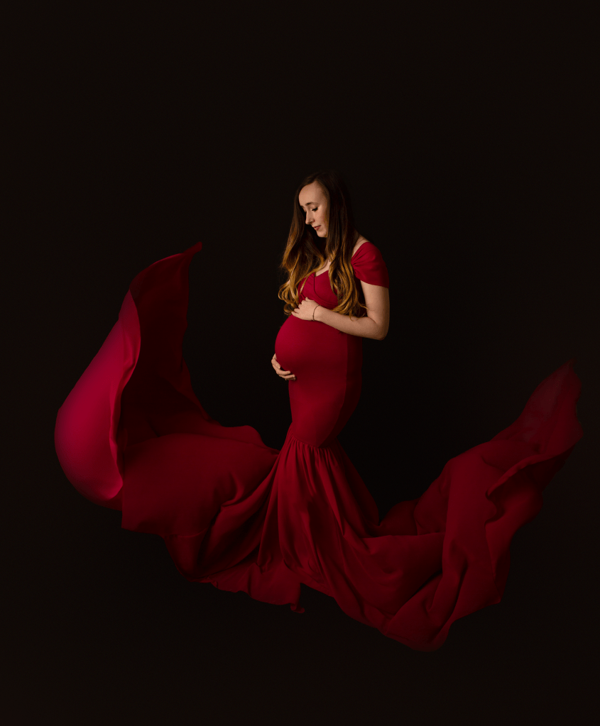 new mother holding her bump wearing a red dress that is floating up in the wind