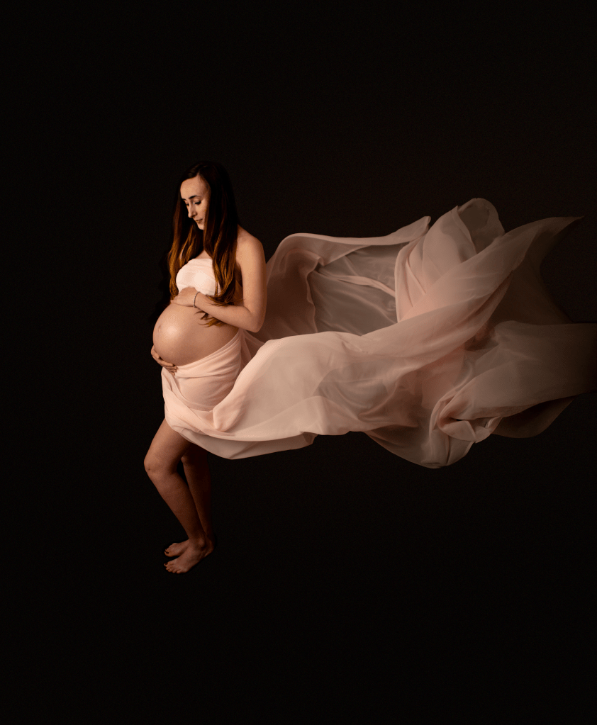 new mother holding her bump wearing a white dress that is blowing in the wind