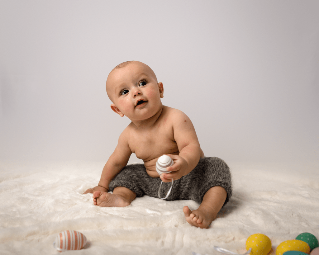 a curious looking baby playing with toy eggs on a fluffy rug
