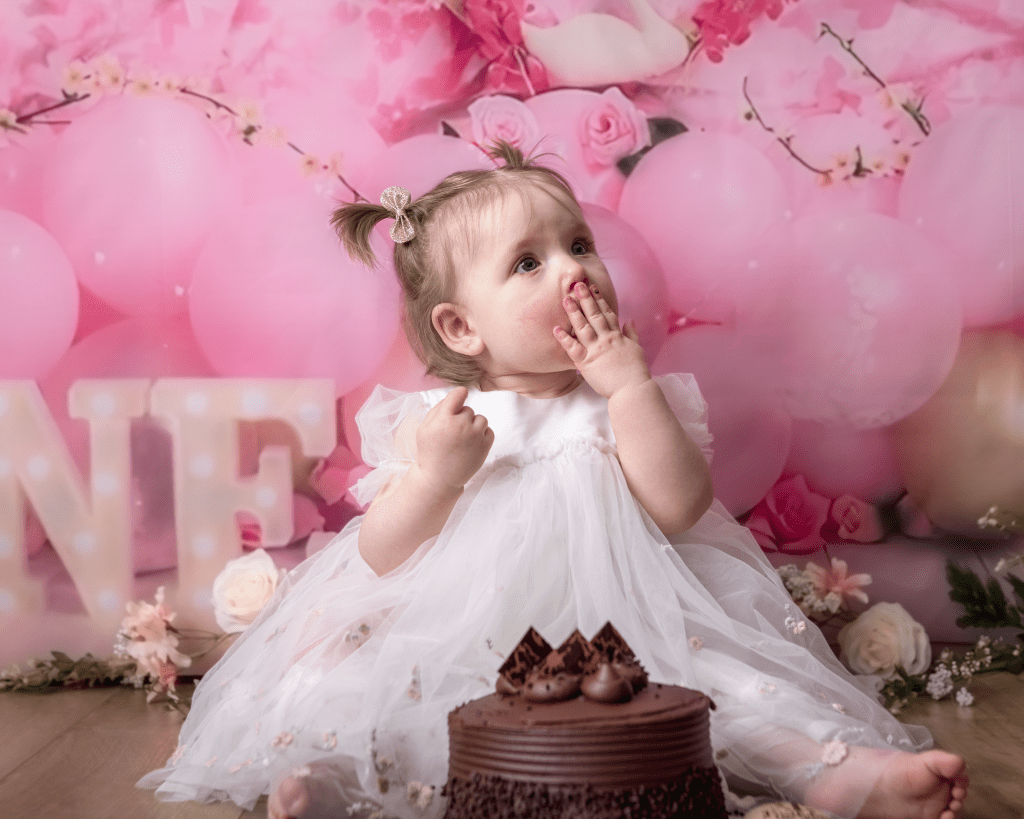 little girl looking guilty in front of a large chocolate cake. She has her hand over her mouth
