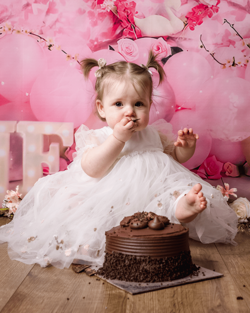 a little girl has taken a handful of chocolate cake and is about to stuff it in her mouth