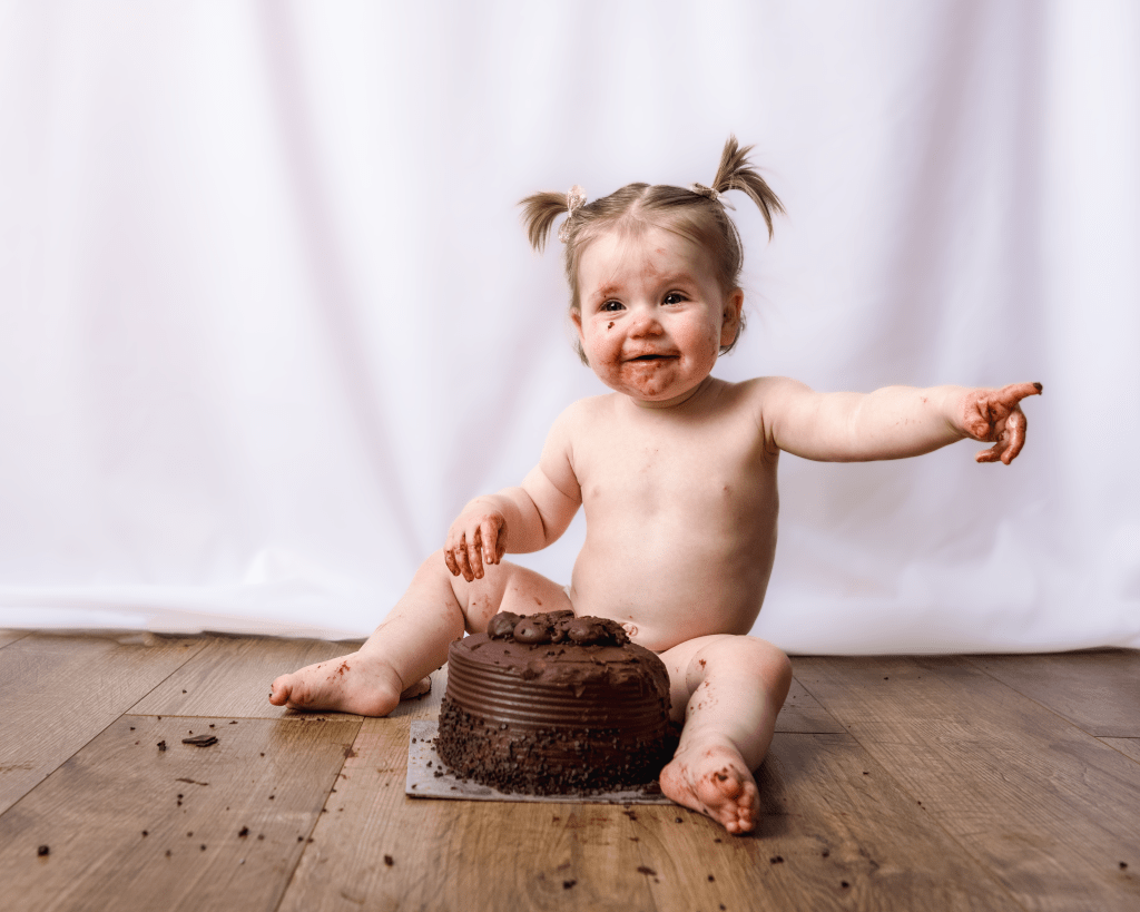 little girl smiling and pointing in front of a chocolate cake