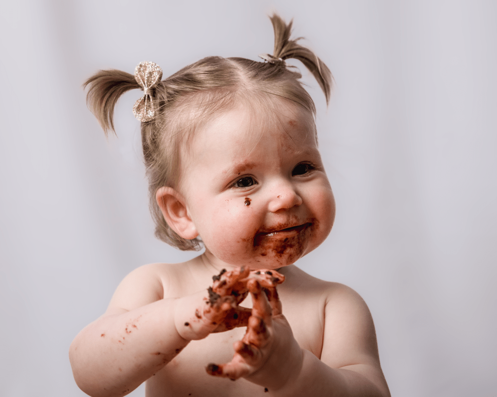 a little girl covered in chocolate cake after smashing it up