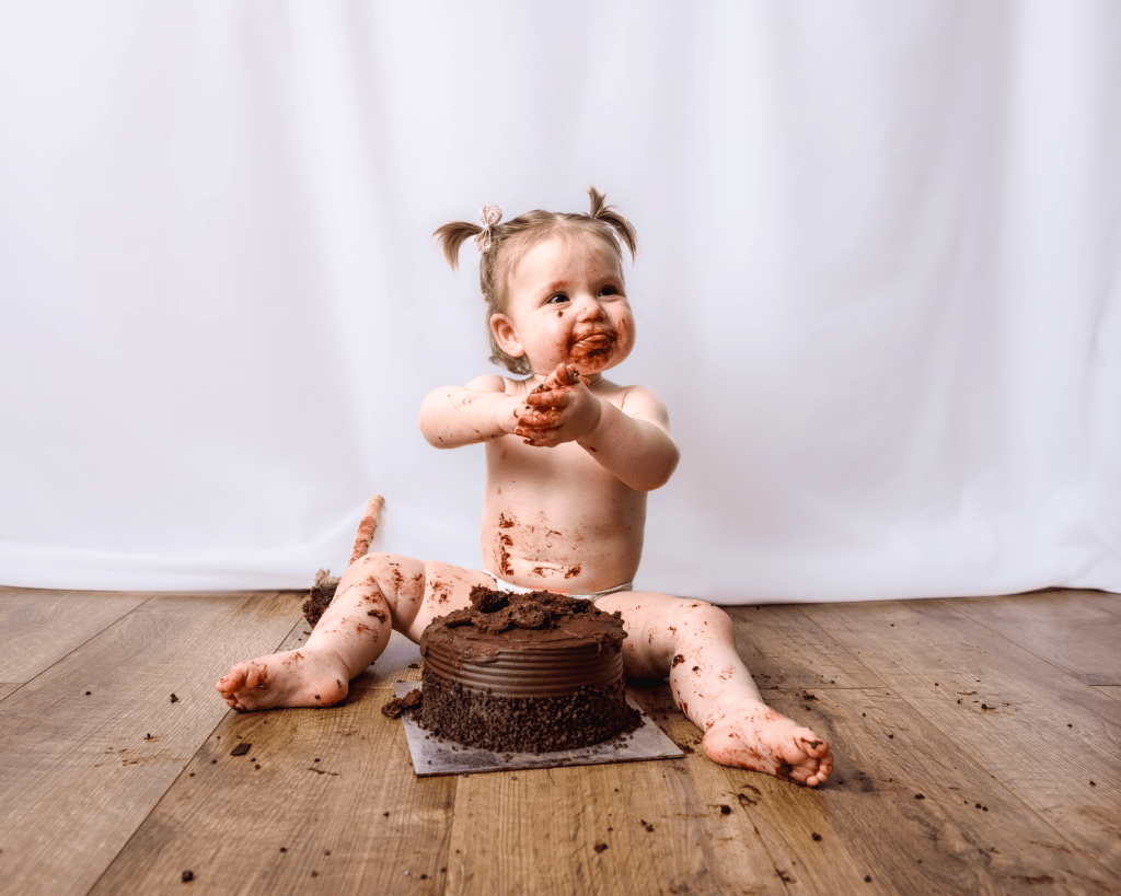 a little girl sits in front of a cake, covered in chocolate cake after smashing it up