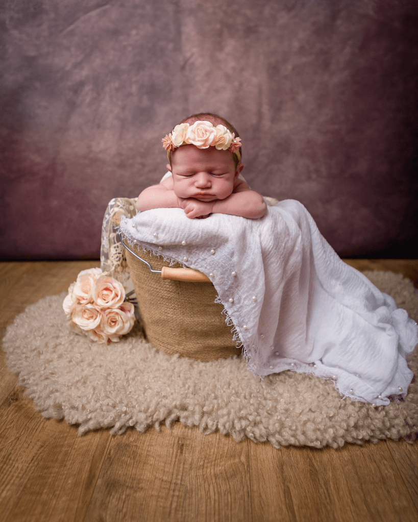 light coloured blanket under a sleeping baby in a basket with light pink flowers and headband