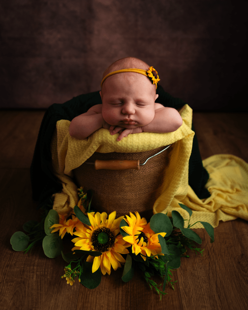 colourful yellow blanket under a sleeping baby in a basket with sunflowers