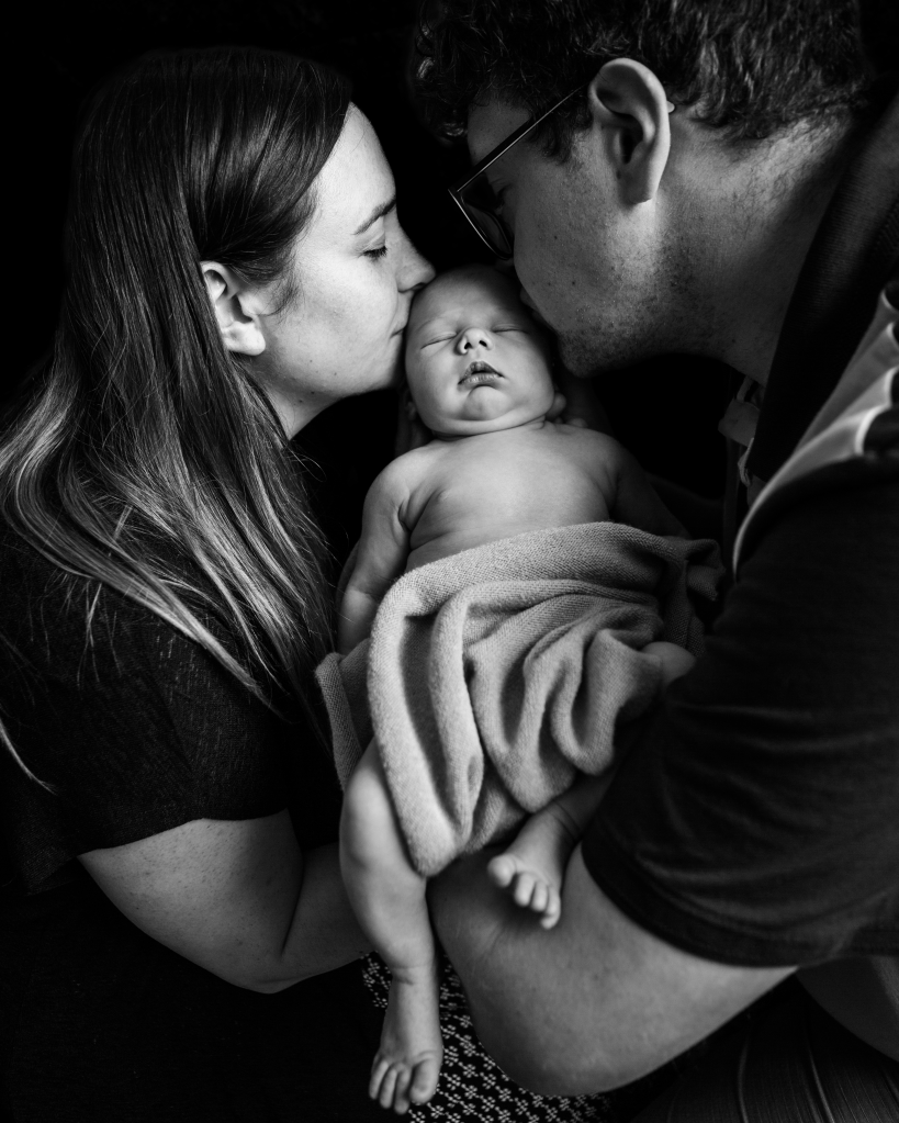 new parents kissing their newborn baby on the forehead together