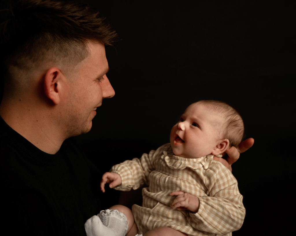 a new father holding up and looking at his newborn baby