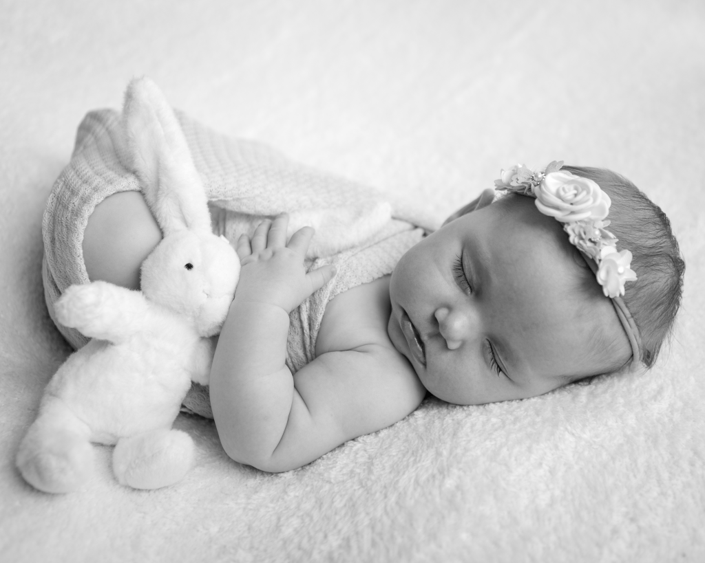 sleeping newborn baby cuddling a white fluffy rabbit